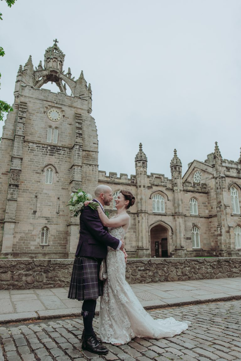 Newly married couple getting their wedding picture taken outside King's College Chapel, Aberdeen: The couple embraces passionately, exuding pure joy and love on their special da