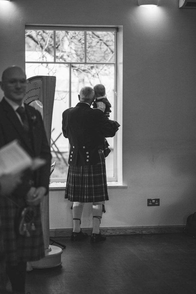 Grandfather and grandson looking out a window at a wedding inside logie country house, Aberdeenshire